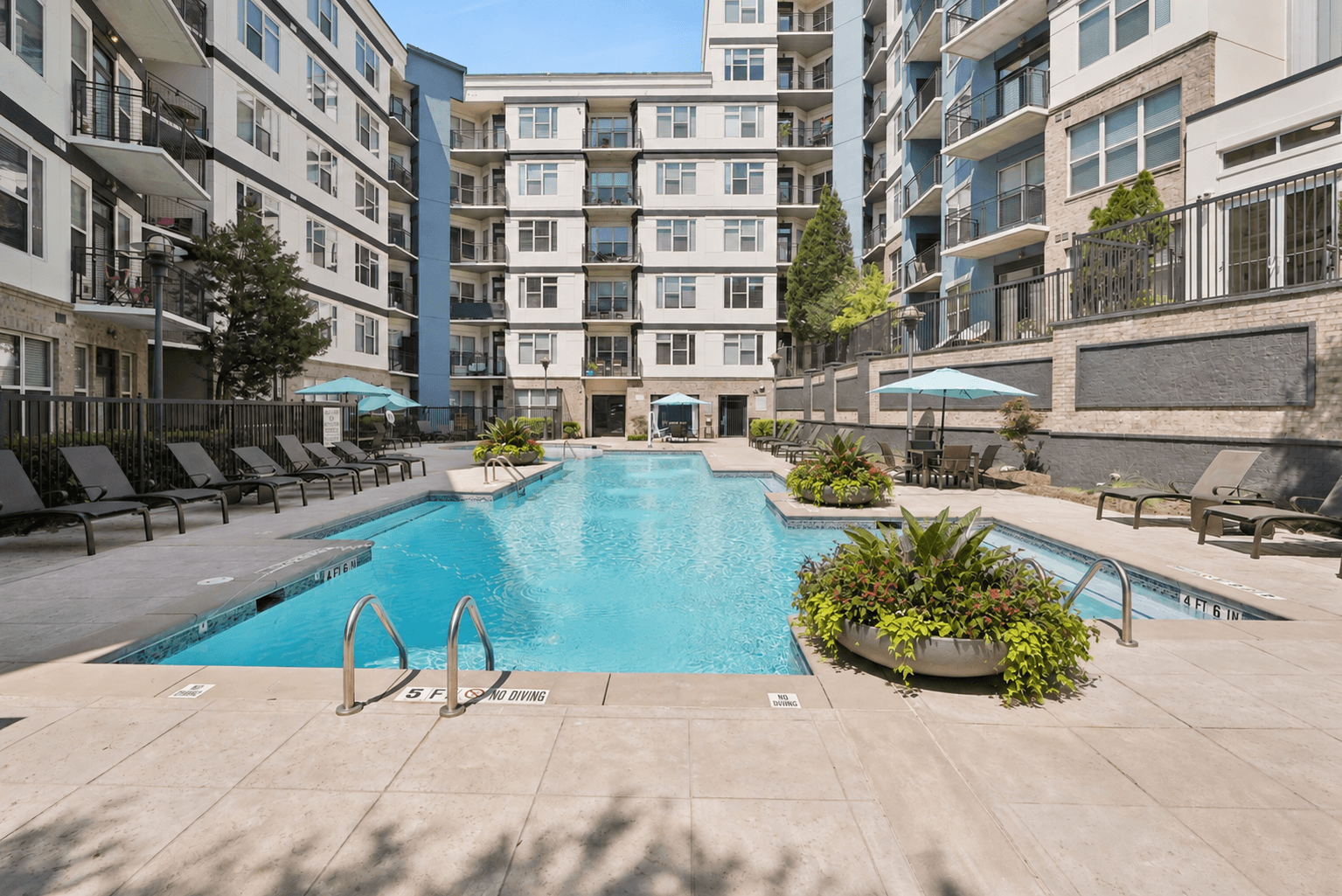 A swimming pool surrounded by lounge chairs and planters in a courtyard.